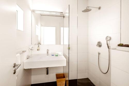 La salle de bains blanche est pourvue d'un lavabo et d'une douche. dans l'établissement Midori - The Green Guesthouse, à Dossenheim