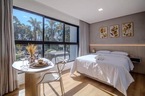 a bedroom with a bed and a table and a large window at Loft Novo todo Mobiliado com WIFI Piscina e próximo a Oktober in Blumenau