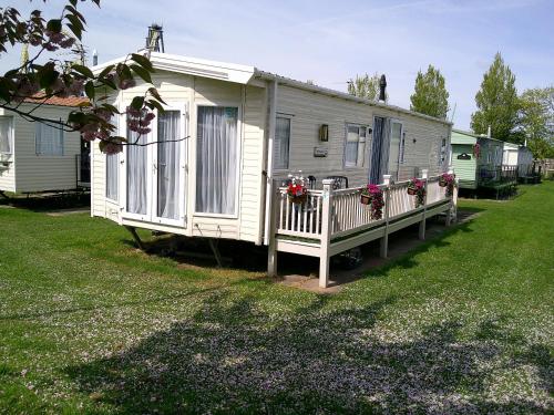 a white mobile home with flowers on a yard at Mayville Parkstone 6 Berth Central heated in Ingoldmells