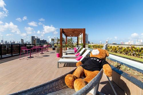 a large teddy bear sitting on a bench on a roof at TOLIVE One Housi Recife by Carpediem in Recife