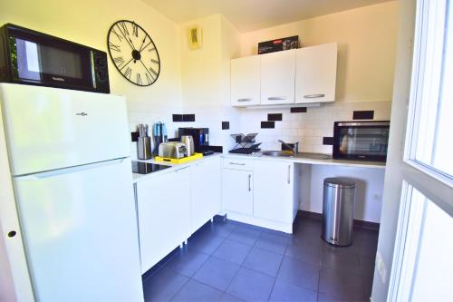 Il comprend une cuisine équipée d'un réfrigérateur blanc et d'une horloge murale. dans l'établissement Le Bicolore Parisien, à Aubervilliers