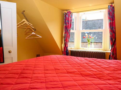 a bedroom with a red bed and a window at Evansford in Ballater