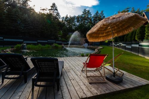 a deck with chairs and an umbrella and a pond at ZIEMIA-OGIEŃ Apartamenty Mazurska Kraina Narie in Bogaczewo
