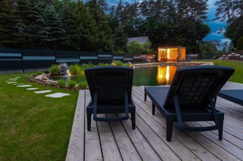 two chairs and a table on a deck near a pond at WIATR Apartamenty Mazurska Kraina Narie in Bogaczewo