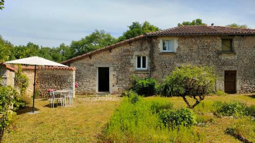 a stone house with a table and an umbrella at Les Murmures de Charente in Villiers-le-Roux
