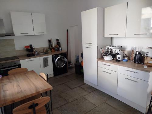 - une cuisine avec des placards blancs, une table et un lave-linge dans l'établissement Maison de village avec terrasse, à Aubais