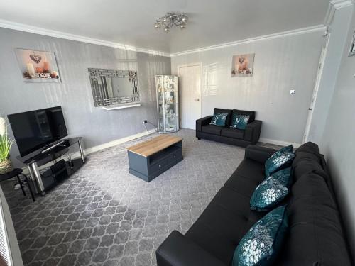 ein Wohnzimmer mit einem schwarzen Sofa und einem TV in der Unterkunft Modern 3-Bed Family Home in Quiet Sheffield Area in Wincobank