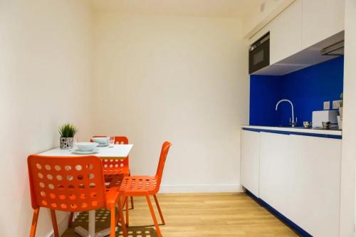 a kitchen with a table with orange chairs and a blue counter at Chapter Aldgate London in London