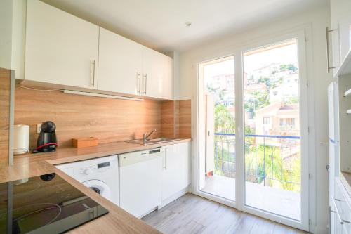 une cuisine avec des placards blancs et une grande fenêtre dans l'établissement Appart vue mer - Proche Monaco, à Beausoleil