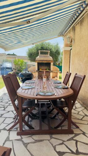 - une table en bois avec des chaises et un barbecue sur la terrasse dans l'établissement Villa L'orée du bois Provence, à Puget-sur Argens