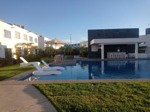 a swimming pool with two white chairs next to a building at Casa Monstera te espera in Naranjo