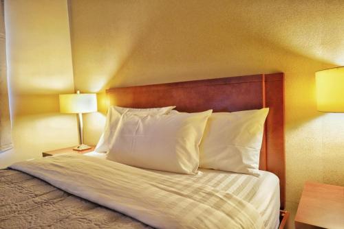a bedroom with a bed with white pillows and two lamps at Hotel Le Mirage in Saint-Basile-le-Grand