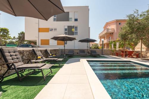 a swimming pool with chairs and umbrellas next to a building at Villa Pagus with pool and private parking in Novalja