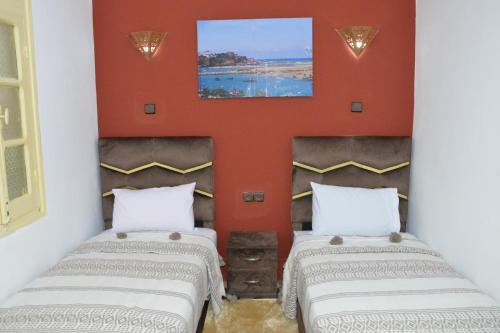 two beds in a room with orange walls at Riad Bladi Essaouira in Essaouira