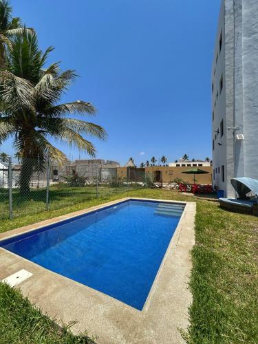 a blue swimming pool with a palm tree and a building at Tritón Apartment, ground floor and pool in Barra de Navidad