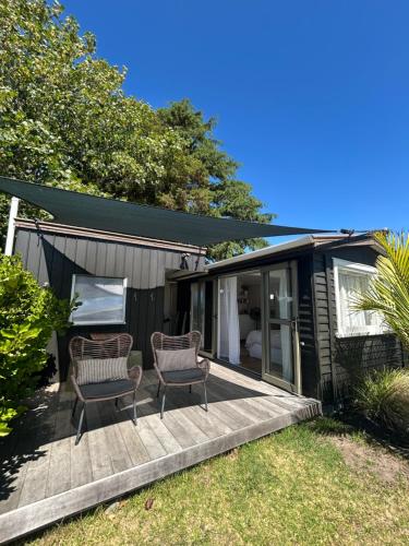 a small house with two chairs on a deck at Cooks Beach Studio Escape in Cooks Beach