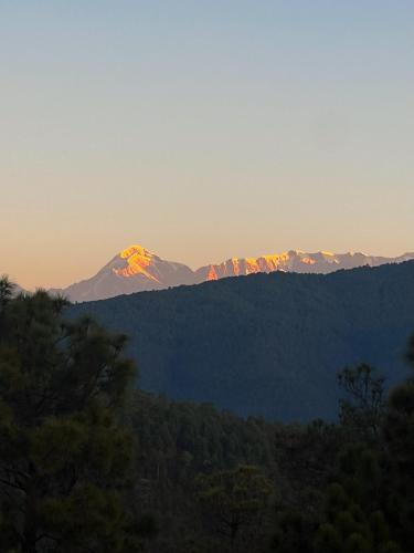 a mountain in the distance with the sun shining on it at Jaadooghar The Chitai Life in Almora