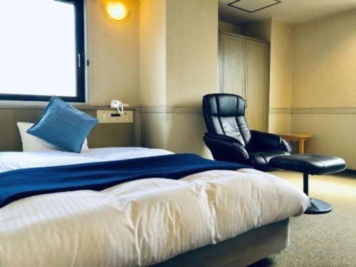 a bedroom with a bed and a black chair at Business Hotel Nishiura Yokkaichi in Yokkaichi