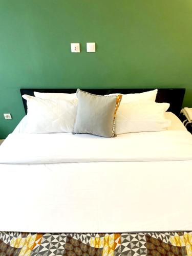 a white bed with white pillows and a green wall at Résidences Les Hauts de l'Indenié in Abidjan
