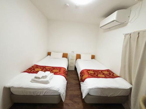 twee bedden in een kleine kamer met witte muren bij 花の郷田端a04 in Tokyo