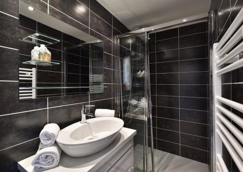 La salle de bains est pourvue de carrelage noir, d'un lavabo et d'une douche. dans l'établissement Studio Glossy Héliopolis AB 325 - 2 personnes, au Cap d'Agde