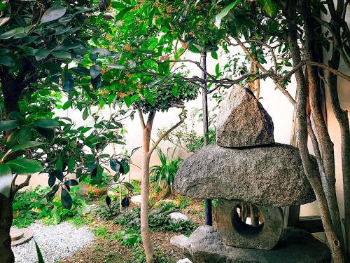 a rock statue sitting next to some trees at 泉庵-奈良と大阪の結び目 小阪に佇む 和のやすらぎ宿 in Osaka