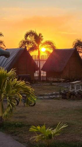 a sunset over a house with palm trees in the background at Good Guys Beach Resort in Botolan