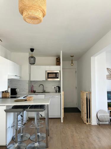 une cuisine avec des armoires blanches et une table avec des tabourets dans l'établissement La Marina-Studio, vue mer avec balneo, à Deauville