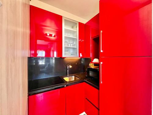 - une cuisine rouge avec évier et réfrigérateur dans l'établissement Superbe appartement face à la mer, à Roquebrune-Cap-Martin
