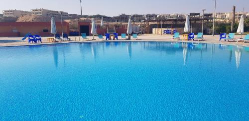 a large blue swimming pool with blue chairs and tables at Koun Ras ElHikma كون راس الحكمة in Ras Elhekma