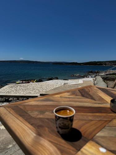 a cup of coffee sitting on a wooden table next to the ocean at Krk Houses in Kornić