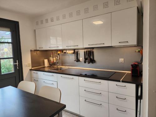 une cuisine avec des armoires blanches et un comptoir noir dans l'établissement Maison entouré par un jardin proche Paris et Disney, à Pontault-Combault