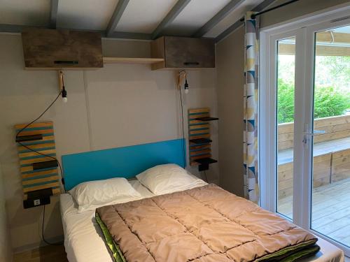 - une chambre avec un lit doté d'une tête de lit bleue et d'une fenêtre dans l'établissement Locations au camping Les Pialades, à Nabirat