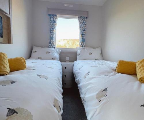two twin beds in a room with a window at Dune Breeze-Haven Perran Sands Holiday Park in Perranporth
