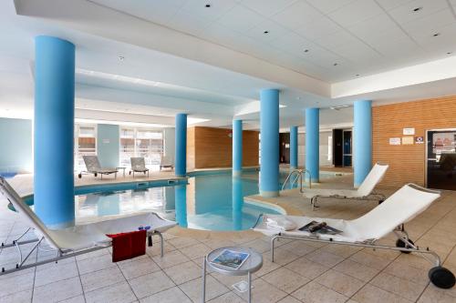 a pool in a building with white chairs and blue columns at Vacancéole - Les Chalets du Verdon in La Foux