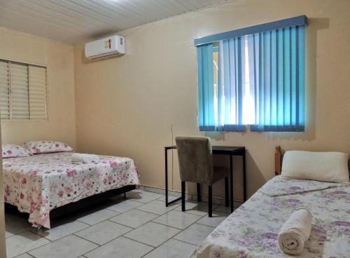 a bedroom with two beds and a desk and a window at Pousada Santa Rita in Abadiânia