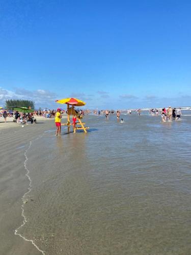 a group of people on a beach with an umbrella at Lindo Apartamento de 2 quartos a 100 metros da praia in Ilha Comprida