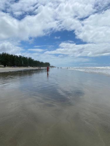 a beach with people standing in the water at Lindo Apartamento de 2 quartos a 100 metros da praia in Ilha Comprida