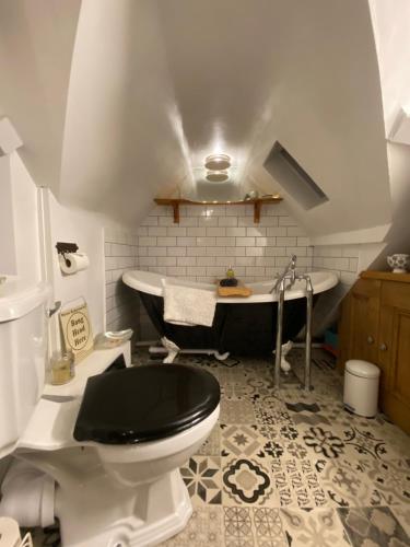 ein Badezimmer mit einem schwarzen WC und einer Badewanne in der Unterkunft St Catherines Cottage The Old Schoolhouse in Long Melford