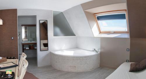 ein Bad mit einer Badewanne und einem Fenster in der Unterkunft Logis Hotel Du Casino Restaurant Le Mathelia in Vierville-sur-Mer