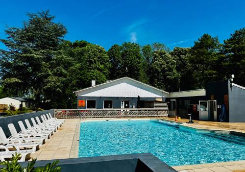 une piscine avec des chaises blanches et une maison dans l'établissement Évasion famille - Dune Blanche, à Camiers