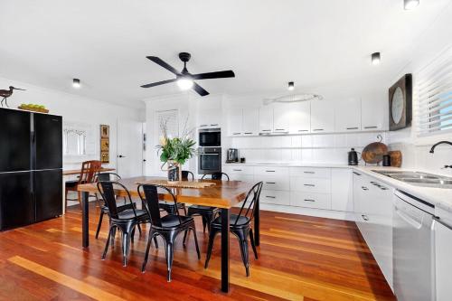 a kitchen with white cabinets and a wooden table and chairs at Quirky Black Shack in Burnett Heads