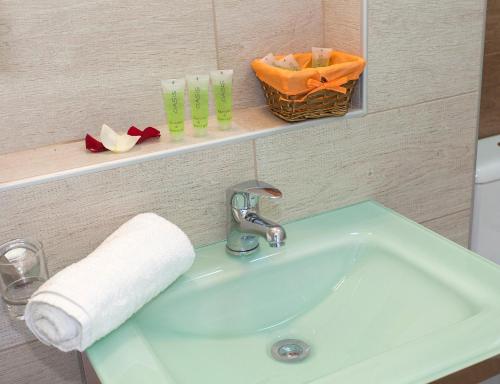 - un lavabo dans la salle de bains avec une serviette et des verres sur une étagère dans l'établissement Oasis Exclusive, à Parga