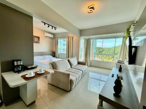 a living room with a couch and a bed and a window at Flat - Frente Mar, Roda Gigante e Estrada da Rainha in Balneário Camboriú