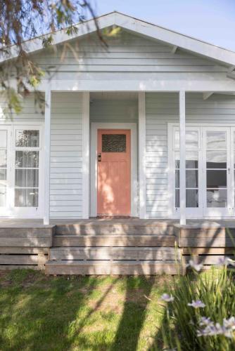 a white house with a wooden porch with a red door at Fitzs Folly in New Plymouth