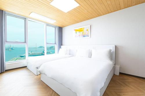 a white bedroom with two beds and a window at Brown Suites Busan Station in Busan