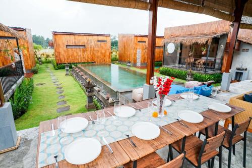 Ein Holztisch mit weißen Tellern darauf neben einem Pool in der Unterkunft Nila Chandra Bungalows in Ubud