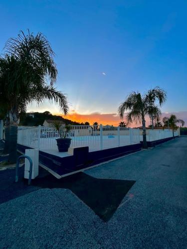 une clôture blanche avec des palmiers et un coucher de soleil dans l'établissement Mobil Home piscine, proche plages, à Fréjus