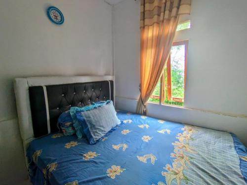 a bed with a blue comforter and a window at Rumah Liburan Sikabu-kabu in Airtabit