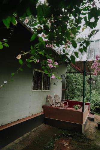 two chairs and a table on a porch with pink flowers at Ela Ecoland Nature Retreat in Munnar